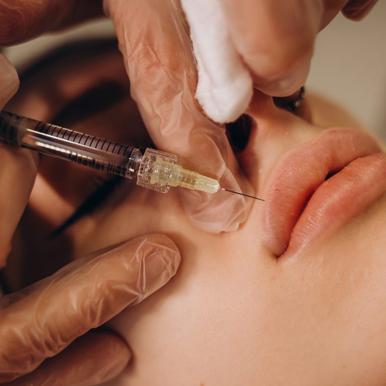Close up of hands of cosmetologist making botox injection in female lips. She is holding syringe. The young beautiful woman is receiving procedure with enjoyment